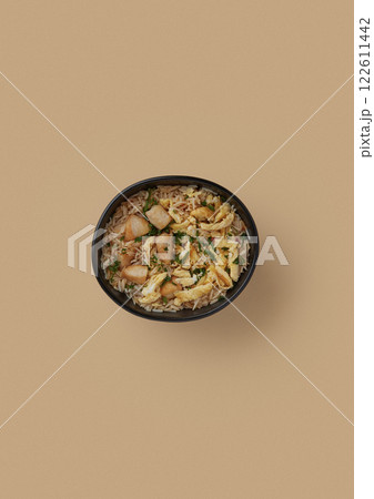 on beige background, a round black plate with fried rice, fried omelette and pieces of chicken fillet sprinkled with finely chopped green onions Chinese cuisine balanced food 122611442