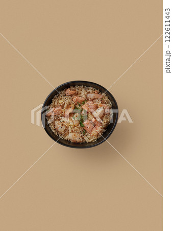 on beige background, a round black plate with fried rice and pieces of tiger shrimp sprinkled with black and white sesame seeds and finely chopped green onions 122611443