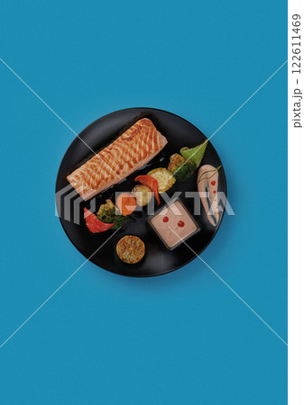 on blue background on a black plate laid out red grilled salmon fillet served with grilled vegetables and additional fish sauce professional cuisine 122611469