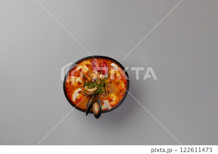 top shot on gray background professional kitchen soup black plate in tom yum tomato sauce white mushrooms assorted seafood japanese traditional cuisine spicy decorated with mussel 122611473
