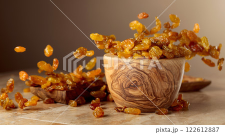 Yellow sultana raisins pour into a wooden bowl. 122612887