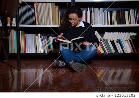 Woman reading a book while sitting on the library floor 122613102