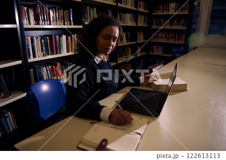 Woman studying in library with a laptop and open books around her 122613113
