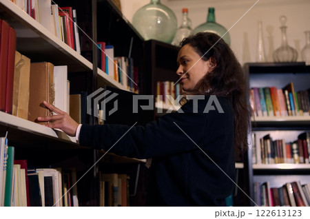 Smiling woman selecting a book from a library shelf in a calm setting Smiling woman selecting a book from a library shelf in a calm setting 122613123