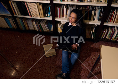 Woman studying with a laptop and book in a library for knowledge 122613137