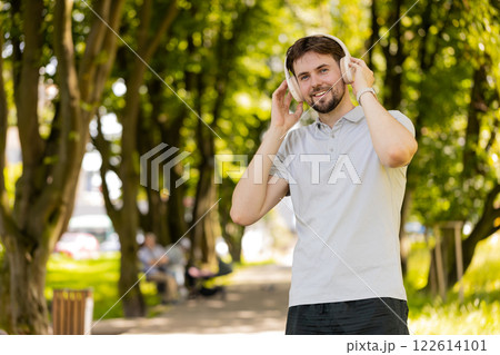 Happy runner jogger smiling man put on wireless headphones earphones enjoy music in park outdoors 122614101