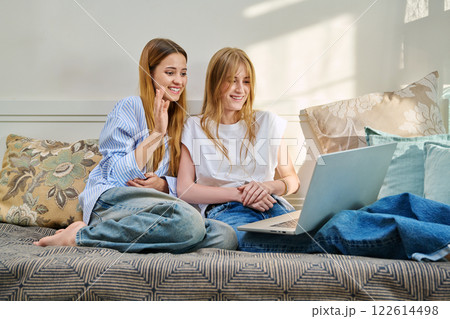 Two young cheerful teenage girls friends students at home looking at laptop, sitting on couch Two young cheerful teenage girls friends students at home looking at laptop, sitting on couch 122614498
