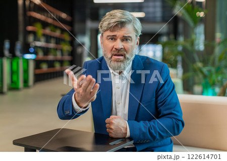 Mature angry boss businessman shouting while looking at camera at modern workplace in office lobby Mature angry boss businessman shouting while looking at camera at modern workplace in office lobby 122614701