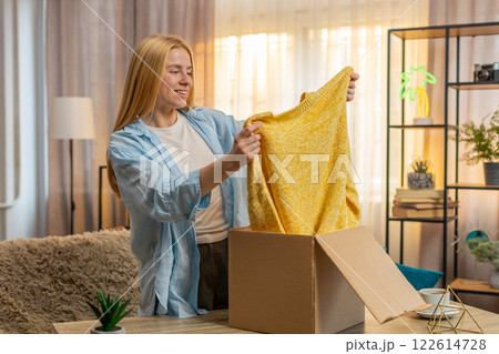 Young woman unboxing package at home, happy find, sofa reveal, smiling display, casual discovery 122614728