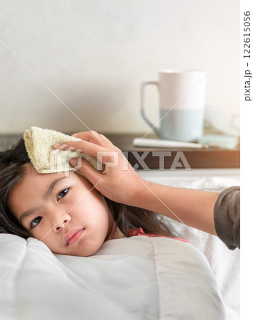 Sick Child Receiving Care From Parent With Cool Cloth on Forehead in Cozy Bedroom Setting 122615056