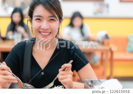 A woman is smiling while eating at a restaurant. She is holding a fork and spoon in her hands A woman is smiling while eating at a restaurant. She is holding a fork and spoon in her hands 122615058