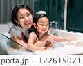 Asian woman and girl are in a bathtub, with the woman smiling and the child laughing. Scene is happy and playful 122615071