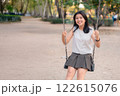 Young Girl Enjoying Sunny Day on Swing in Park Surrounded by Green Trees and Pathway 122615076