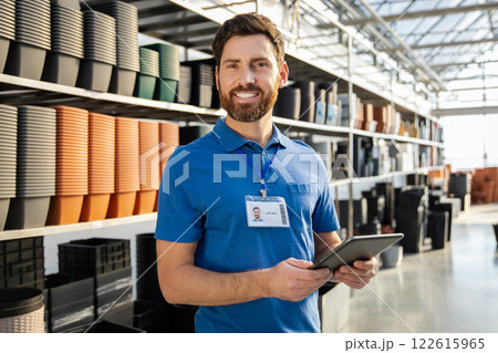 Man worker in greenhouse selling pots for plants standing on racks indoors garden center 122615965