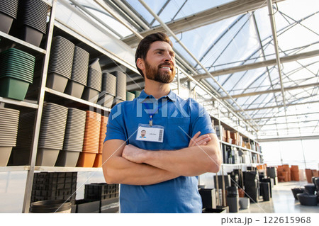 Man worker in greenhouse selling pots for plants standing on racks indoors garden center Man worker in greenhouse selling pots for plants standing on racks indoors garden center 122615968