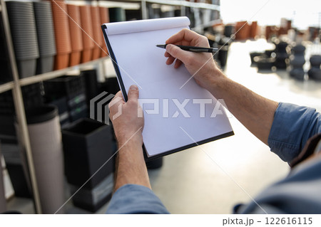 Male owner of small business accounting pots in warehouse on shelves in store 122616115