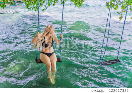 Beautiful female tourist relaxing on a swing in Laguna Bacalar in Mexico during kayak trip. Female tourist swinging over Lake Bacalar with feet in the water. Quintana Roo, Mexico travel, relaxation 122617383