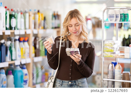 Girl housewife in household store examines goods, chooses candle Girl housewife in household store examines goods, chooses candle 122617693