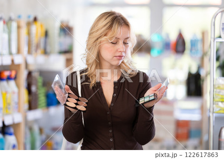 Nice young girl thinking and choosing face powder and eye shadow in cosmetics department in hypermarket 122617863