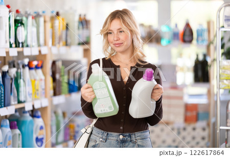 Pretty happy young woman customer buying detergent and choosing between two bottle in store Pretty happy young woman customer buying detergent and choosing between two bottle in store 122617864