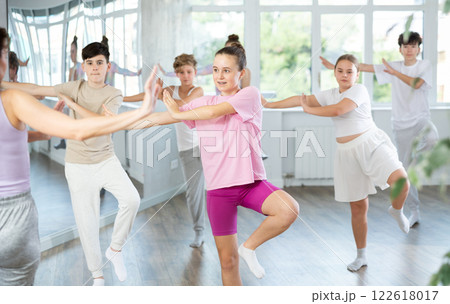 Female girl student repeats movements of unrecognizable teacher during group modern dance class. 122618017