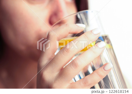 A young woman drinks water with lemon from a transparent glass A young woman drinks water with lemon from a transparent glass 122618154