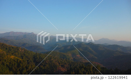 Beautiful sunrise on the mountain with fog in winter. The sun shines down on a serene mountain landscape covered with tropical trees in the early morning. 122619941