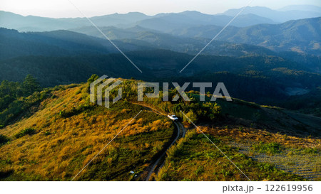 Aerial view of car on rural road driving through tropical forest and mountains in the evening. 122619956