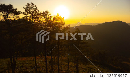 Beautiful sunset in the winter mountains. The setting sun shines down on a serene mountain landscape covered with tropical trees in the evening. Beautiful sunset in the winter mountains. The setting sun shines down on a serene mountain landscape covered with tropical trees in the evening. 122619957