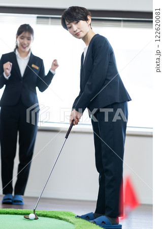 室内でパターを練習している女性社長とヨイショする若手社員 122620081