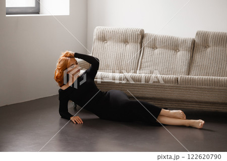 Redhead woman in black dress posing near striped sofa in modern interior 122620790