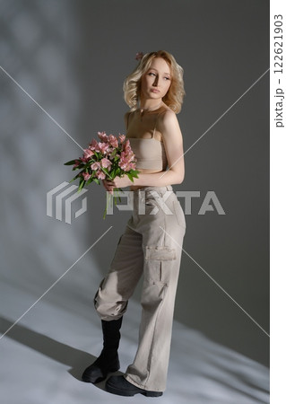 Model poses elegantly with flowers in a stylish indoor setting Model poses elegantly with flowers in a stylish indoor setting 122621903
