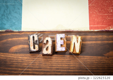 CAEN. Flag and alphabet letters on wooden texture background 122623120