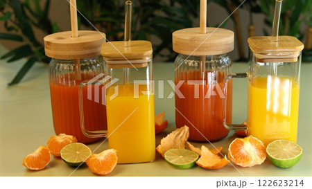 Glass jars with fresh juices placed alongside orange slices, raspberries, and lime peels highlight zero-waste nutrition with eco-conscious containers. Natural balance focus. 122623214