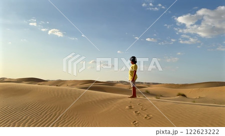 Desert sand ripples beneath child in yellow shirt soft sunlight falls across golden dunes footprints trailing behind as distant horizon meets clear blue sky peaceful adventure concept. 122623222