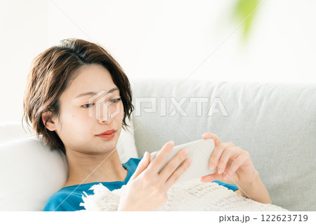 寝転んでスマホを見る若い女性 122623719