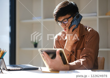 Business professional consulting on phone while using a tablet and reviewing financial documents. Business professional consulting on phone while using a tablet and reviewing financial documents. 122624978