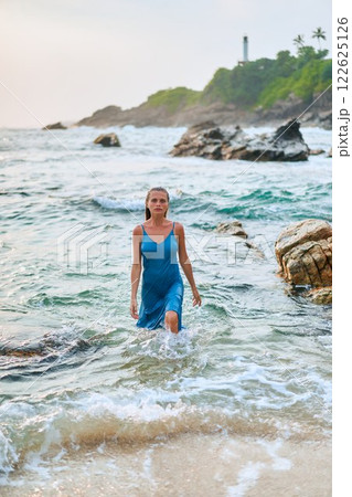 Model in wet dress exits ocean on exotic island. Luxury travel, romantic getaway vibe. Perfect for honeymoon, fashion ads, perfume campaigns. Beautiful woman, beach, ocean, style. Model in wet dress exits ocean on exotic island. Luxury travel, romantic getaway vibe. Perfect for honeymoon, fashion ads, perfume campaigns. Beautiful woman, beach, ocean, style. 122625126