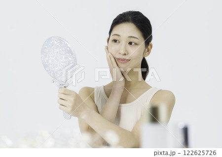 白バックのタンクトップを着て鏡を見ながら手を頬に当てる笑顔の若い女性 ビューティー 白バックのタンクトップを着て鏡を見ながら手を頬に当てる笑顔の若い女性 ビューティー 122625726