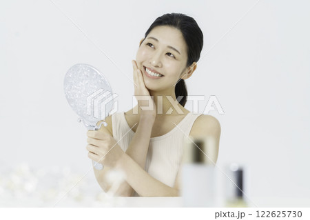 白バックのタンクトップを着て指を頬に当てる笑顔の若い女性 ビューティー 白バックのタンクトップを着て指を頬に当てる笑顔の若い女性 ビューティー 122625730