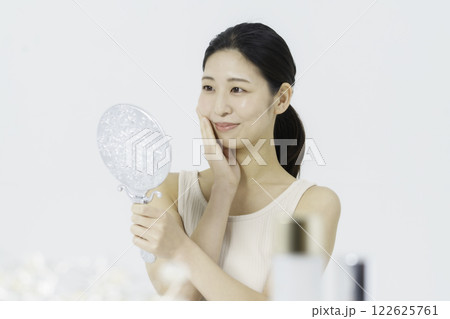 白バックのタンクトップを着て鏡を見ながら手を頬に当てる笑顔の若い女性 ビューティー 白バックのタンクトップを着て鏡を見ながら手を頬に当てる笑顔の若い女性 ビューティー 122625761