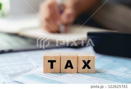 Man is calculating annual tax with calculator with TAX text on wooden block 122625781