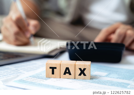 Man is calculating annual tax with calculator with TAX text on wooden block 122625782