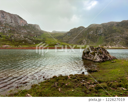 Tranquil mountain lake with rock and green hills under overcast sky 122627019