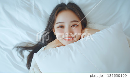 若くてかわいい笑顔のアジア人女性が、ベッドで横になって寝ている。	 122630199