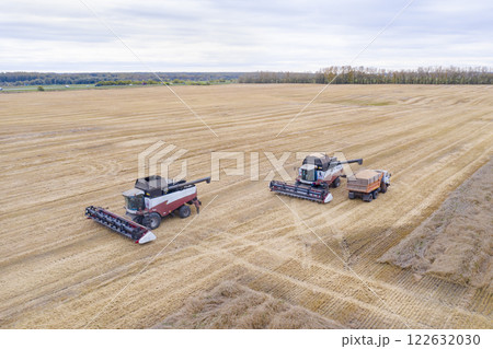 Aerial view of truck filled with grain and agricultural combine harvesters in large field in autumn Aerial view of truck filled with grain and agricultural combine harvesters in large field in autumn 122632030
