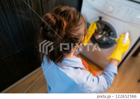 Housekeeper cleaning the kitchen with eco-friendly cleaning products, ensuring the washing machine is free from bacteria, mold, and allergens. 122632366