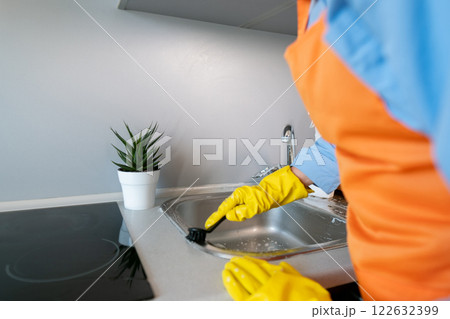 A housewife cleans the sink with a brush; cleaning products help eliminate unpleasant odors like food or garbage smells in the sink. A housewife cleans the sink with a brush; cleaning products help eliminate unpleasant odors like food or garbage smells in the sink. 122632399