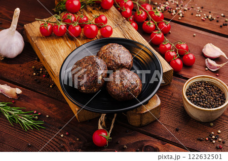 Savory meatballs served on a black plate with fresh herbs and tomatoes on a rustic wooden table 122632501