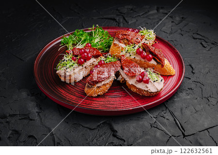 Savory bread slices topped with sun-dried tomatoes, sprouts, and red currants served on a vibrant plate 122632561
